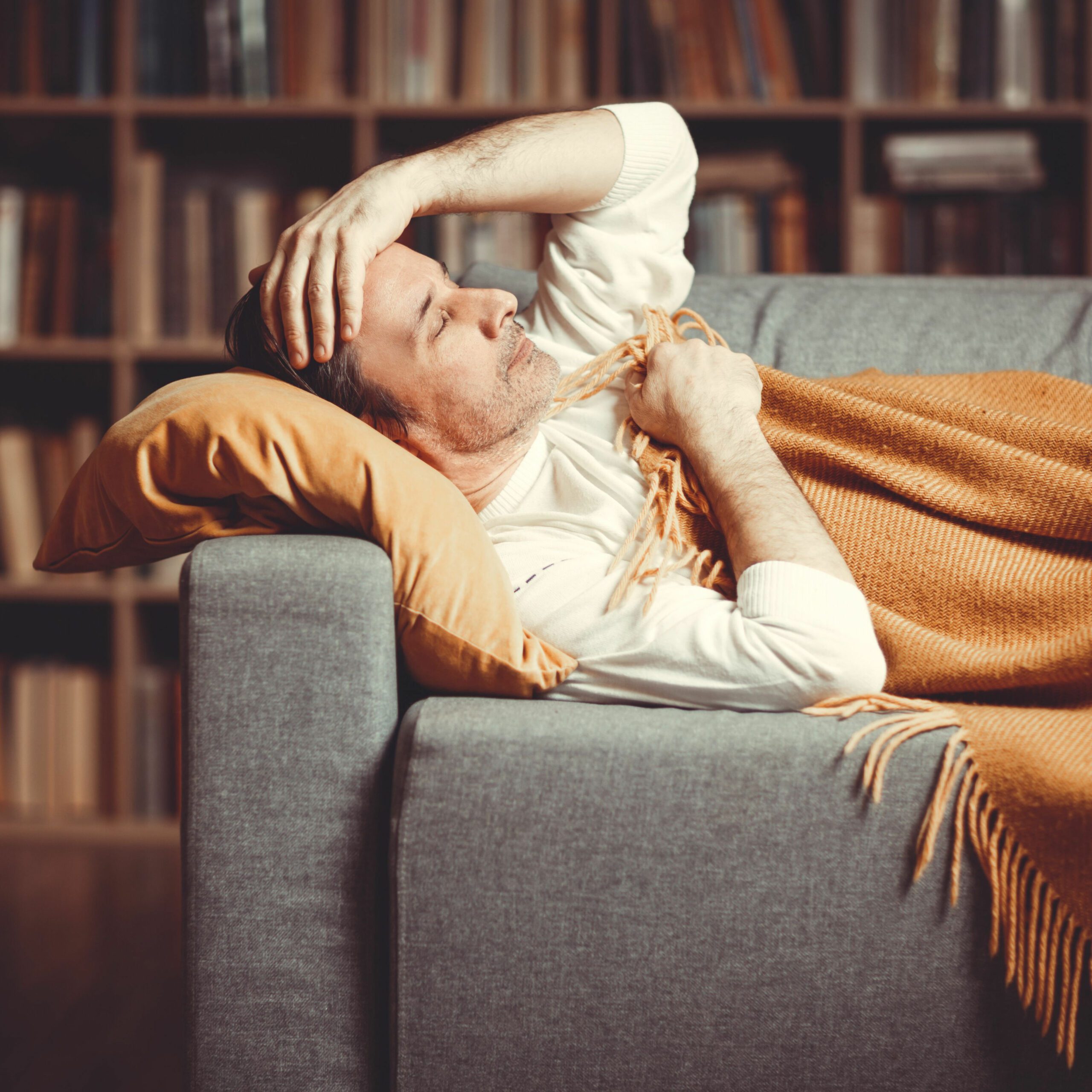 Man laying on a sofa feeling unwell and keeping his hand on the forehead