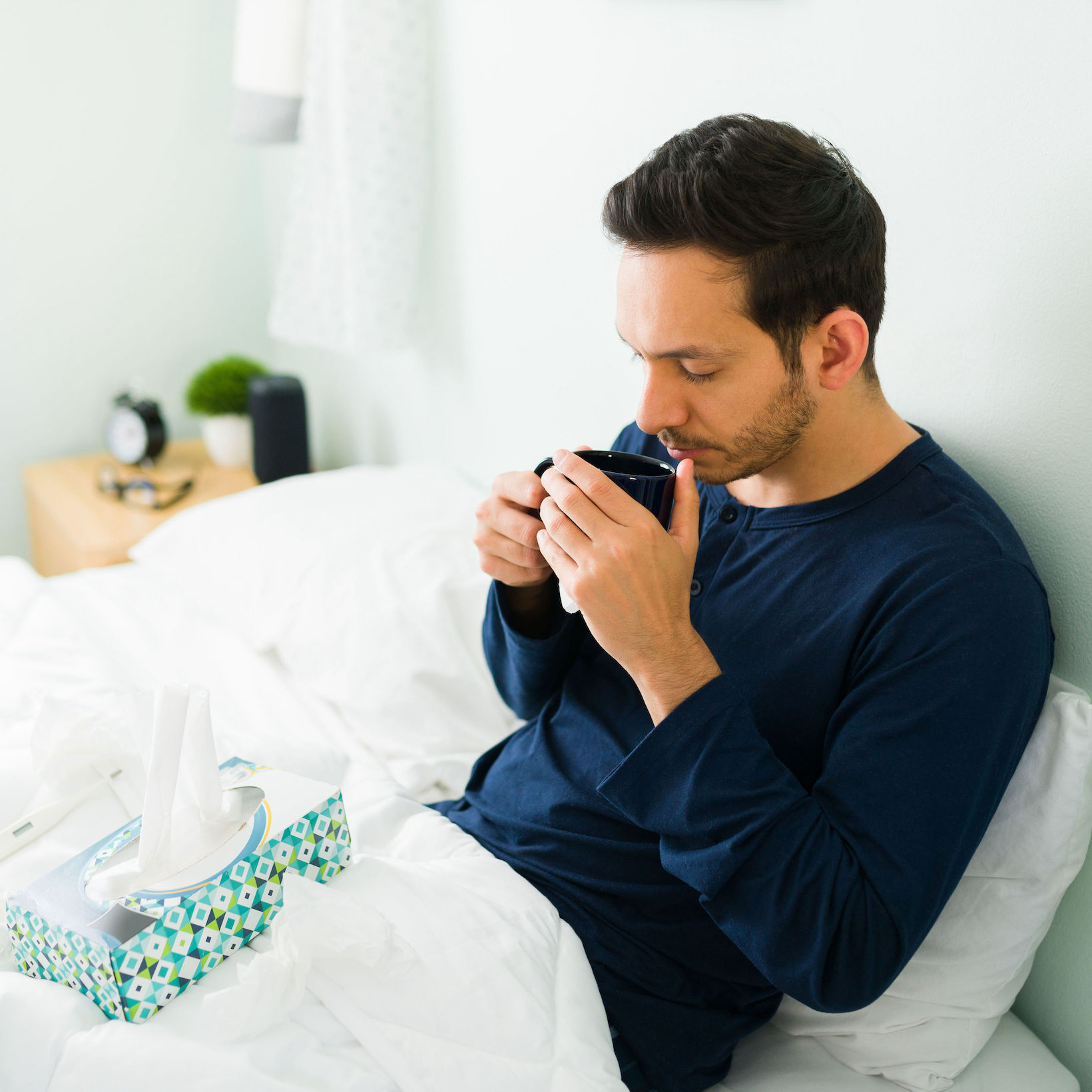 Man with cold sipping tea and having tissues within reach