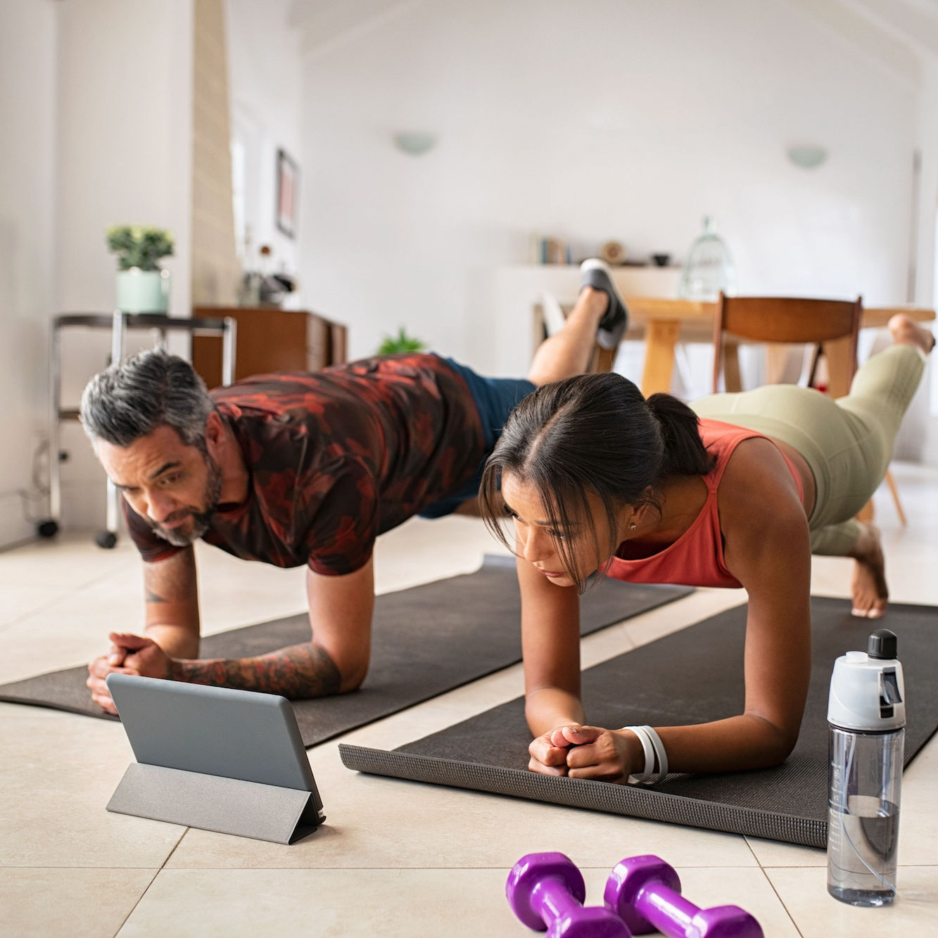 A couple doing a plank at home in front of a tablet