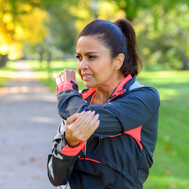 Adult woman holding her painful elbow after exercising in park